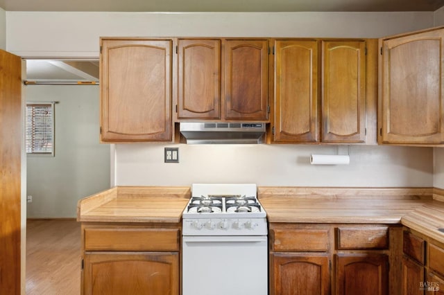 kitchen featuring brown cabinetry, light wood-style floors, light countertops, under cabinet range hood, and gas range gas stove