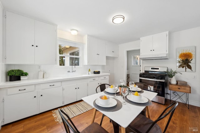 kitchen featuring white cabinets, wood finished floors, under cabinet range hood, light countertops, and stainless steel range oven