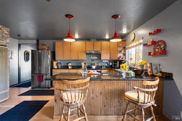 kitchen featuring light wood-style flooring, under cabinet range hood, appliances with stainless steel finishes, open shelves, and dark countertops