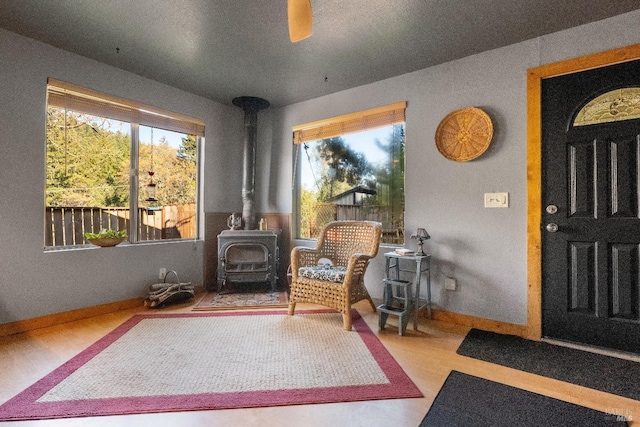 interior space with a wood stove, ceiling fan, baseboards, and wood finished floors