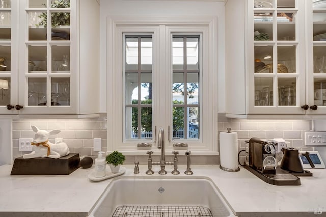 details with glass insert cabinets, white cabinetry, a sink, and backsplash