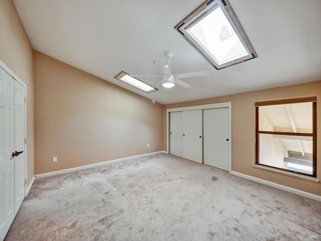 interior space featuring vaulted ceiling with skylight, baseboards, ceiling fan, and carpet flooring