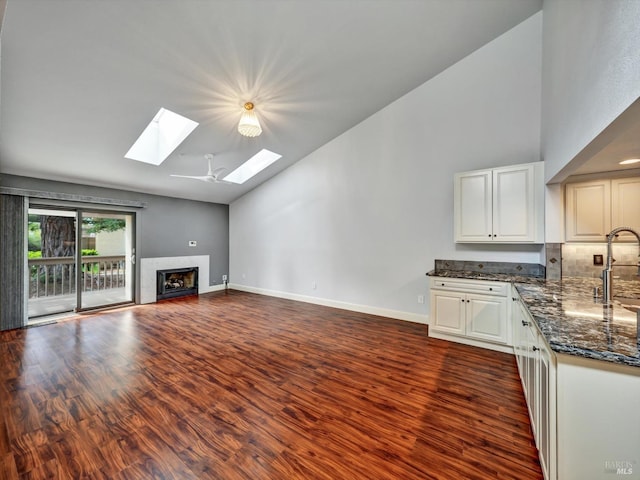 unfurnished living room with a skylight, a fireplace, dark wood finished floors, and baseboards