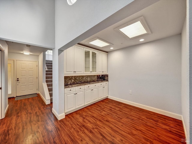 kitchen with baseboards, dark wood-type flooring, glass insert cabinets, and white cabinetry