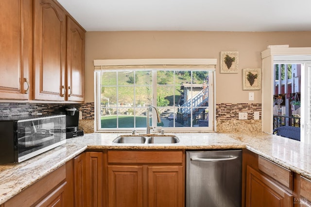 kitchen with tasteful backsplash, stainless steel dishwasher, brown cabinetry, a sink, and light stone countertops