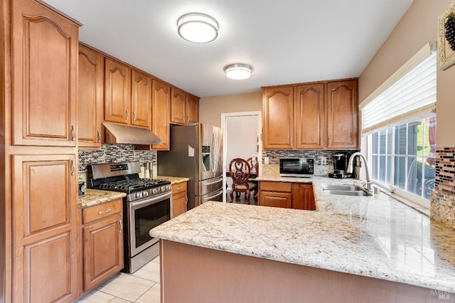 kitchen featuring appliances with stainless steel finishes, a sink, a peninsula, light stone countertops, and under cabinet range hood