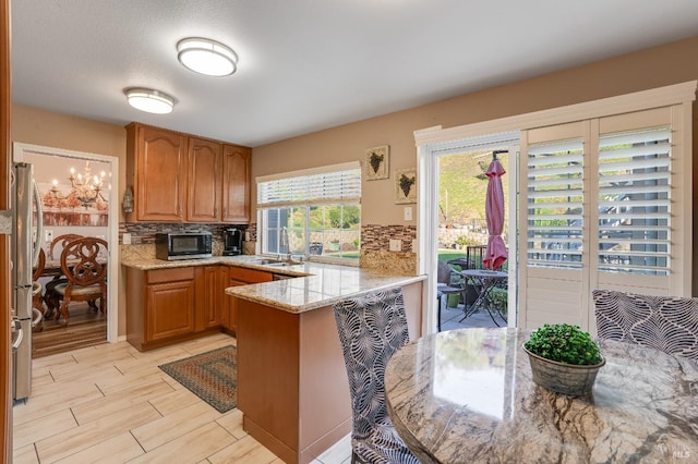 kitchen featuring a sink, backsplash, a peninsula, and light stone countertops