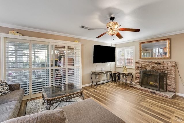 living area featuring a brick fireplace, visible vents, crown molding, and wood finished floors