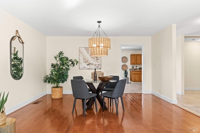 dining area featuring visible vents, a notable chandelier, baseboards, and wood finished floors