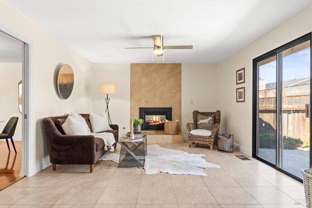 living area with light tile patterned floors, a tile fireplace, visible vents, baseboards, and a ceiling fan