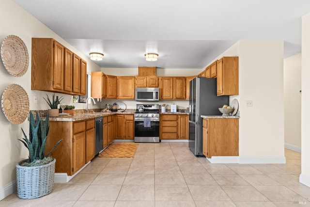 kitchen featuring stainless steel appliances, brown cabinets, a sink, and light stone countertops