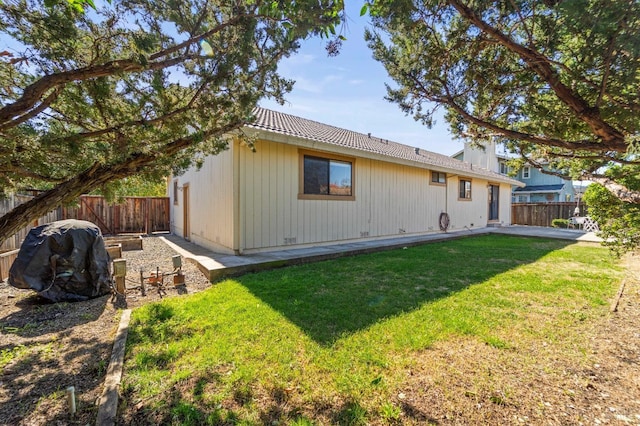 rear view of property featuring a yard, a fenced backyard, and a tiled roof