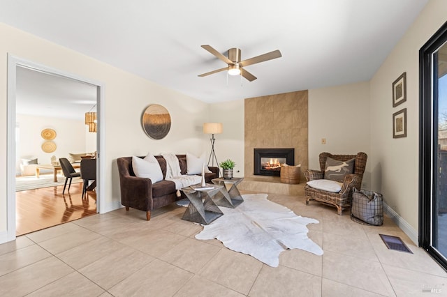 living room featuring light tile patterned floors, ceiling fan, a tile fireplace, visible vents, and baseboards