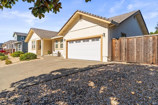 view of front of house featuring driveway, a tiled roof, an attached garage, and fence