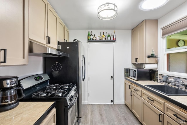 kitchen featuring a sink, tasteful backsplash, under cabinet range hood, stainless steel appliances, and light wood-style floors