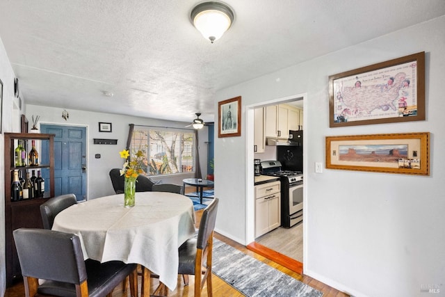 dining room with a ceiling fan, light wood-style flooring, baseboards, and a textured ceiling