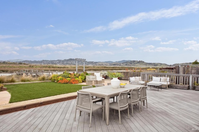 wooden terrace featuring outdoor lounge area, a lawn, outdoor dining space, a mountain view, and fence