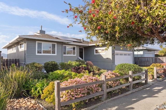 single story home featuring solar panels, a chimney, an attached garage, and fence