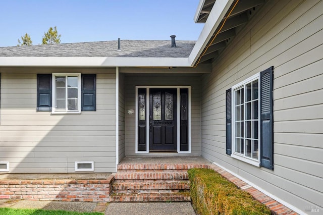 view of exterior entry featuring a shingled roof