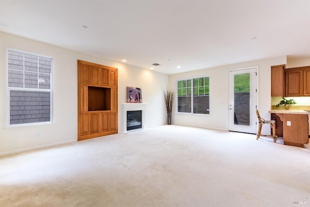 unfurnished living room with a glass covered fireplace, light carpet, baseboards, and recessed lighting