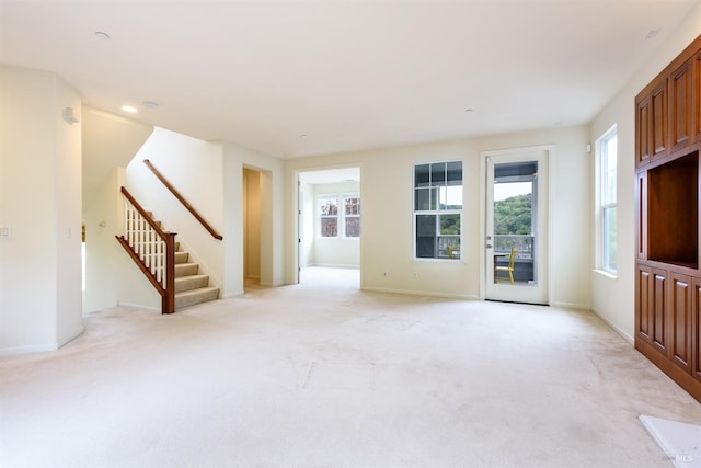 unfurnished living room with baseboards, stairway, and light colored carpet