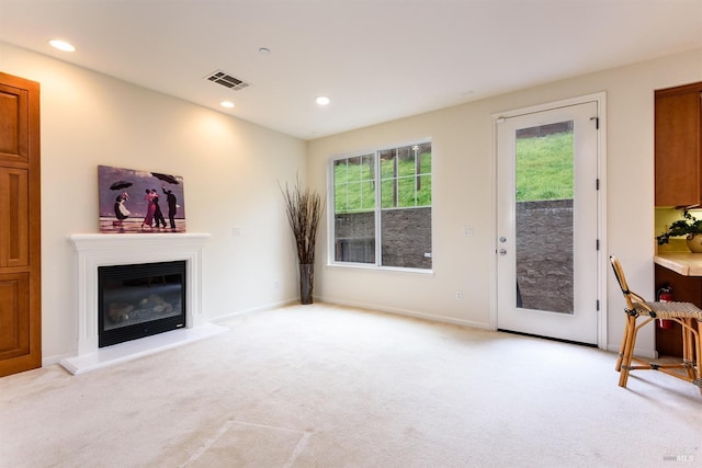 living room featuring recessed lighting, a glass covered fireplace, visible vents, and light colored carpet