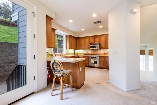 kitchen featuring visible vents, light colored carpet, brown cabinets, a peninsula, and stainless steel appliances