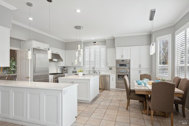 kitchen with light countertops, hanging light fixtures, appliances with stainless steel finishes, a kitchen island, and under cabinet range hood