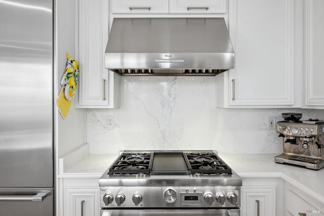 kitchen featuring tasteful backsplash, white cabinets, appliances with stainless steel finishes, light stone countertops, and wall chimney range hood