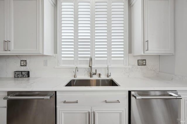 kitchen featuring light stone counters, white cabinets, a sink, and stainless steel dishwasher