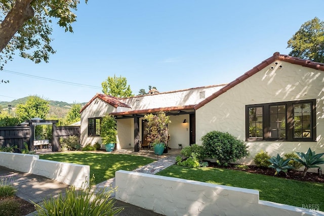 view of front facade featuring a tiled roof, fence, a mountain view, a front lawn, and stucco siding