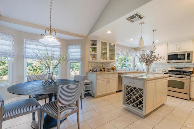 kitchen with a center island, pendant lighting, stainless steel appliances, visible vents, and glass insert cabinets