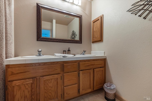 bathroom with a textured wall, double vanity, a sink, and visible vents