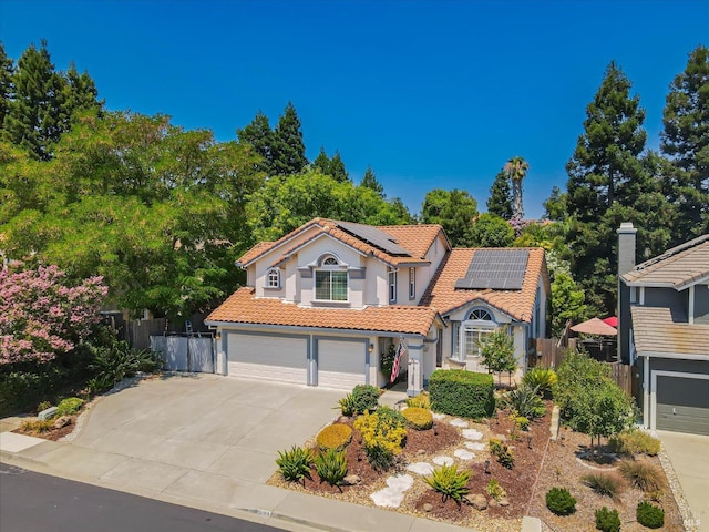 mediterranean / spanish home featuring a garage, driveway, solar panels, a tile roof, and fence