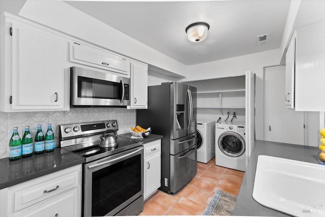 kitchen with stainless steel appliances, dark countertops, washing machine and dryer, and white cabinetry