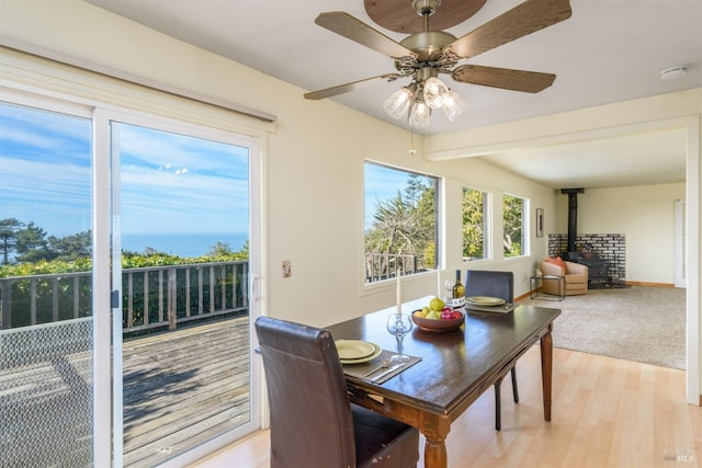 dining space featuring baseboards, light wood-type flooring, a wood stove, and a ceiling fan