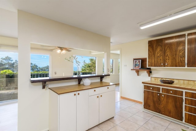 kitchen featuring a ceiling fan, white cabinets, baseboards, and light tile patterned flooring