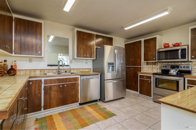 kitchen with light tile patterned floors, decorative backsplash, appliances with stainless steel finishes, dark brown cabinets, and a sink