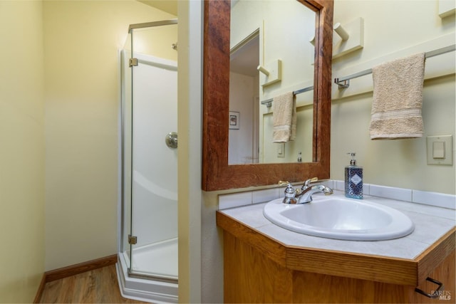 bathroom featuring wood finished floors, a shower stall, vanity, and baseboards