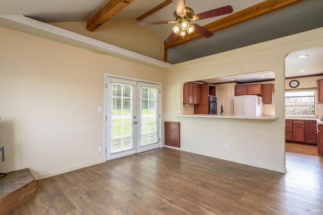 unfurnished living room with dark wood finished floors, french doors, a healthy amount of sunlight, and vaulted ceiling with beams