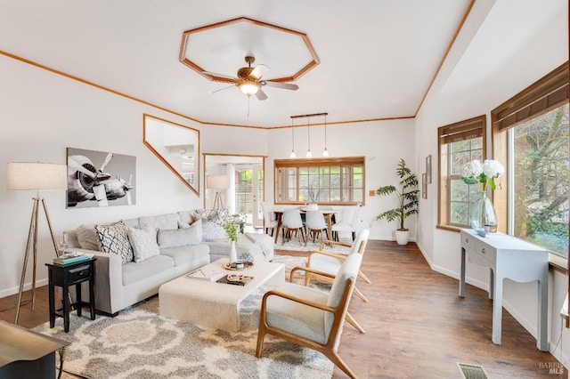 living room featuring lofted ceiling, ornamental molding, ceiling fan, wood finished floors, and baseboards