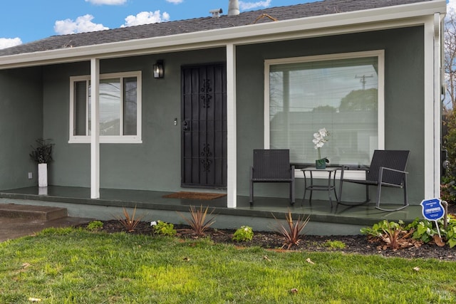 view of exterior entry featuring covered porch, roof with shingles, a yard, and stucco siding