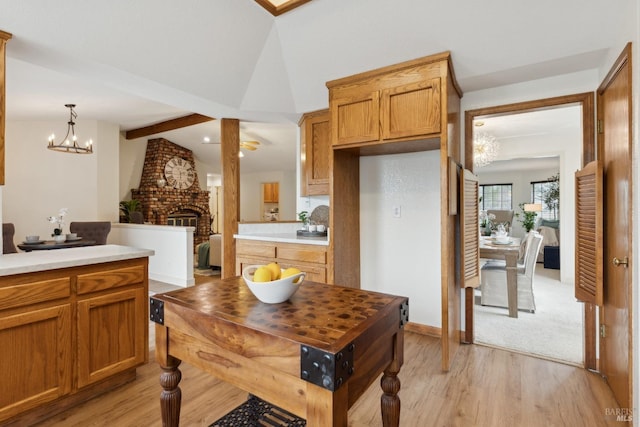 kitchen featuring lofted ceiling with beams, light countertops, light wood-style floors, a fireplace, and pendant lighting