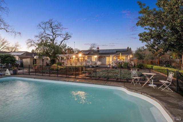 pool at dusk with a patio area, fence, and a fenced in pool