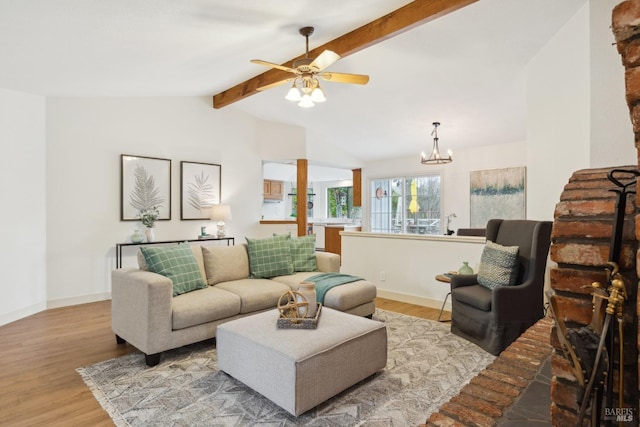 living area with vaulted ceiling with beams, ceiling fan with notable chandelier, light wood-style flooring, and baseboards