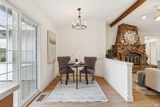 dining room featuring lofted ceiling with beams, visible vents, baseboards, light wood-type flooring, and a brick fireplace