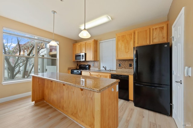 kitchen featuring black appliances, light wood-style flooring, a sink, tasteful backsplash, and a center island