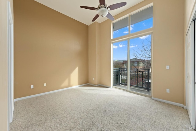 empty room featuring carpet flooring, a ceiling fan, baseboards, and a towering ceiling