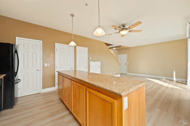 kitchen with light stone countertops, light wood-style floors, freestanding refrigerator, and a kitchen island