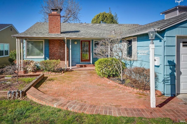 entrance to property featuring brick siding, a chimney, and roof with shingles